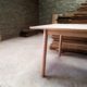 Pale wooden table leg detail with round section legs, stacked timber in the background.