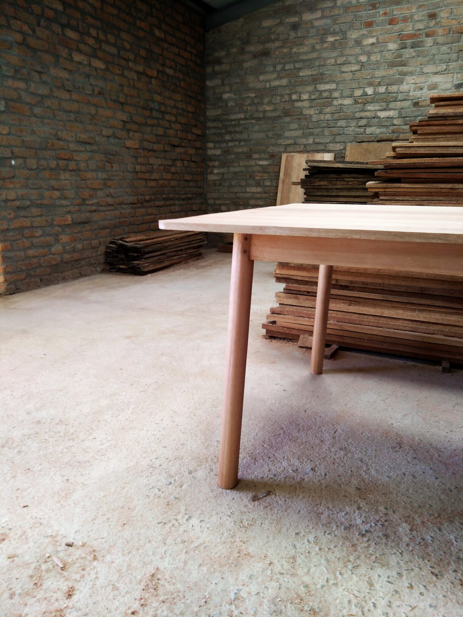 Pale wooden table leg detail with round section legs, stacked timber in the background.