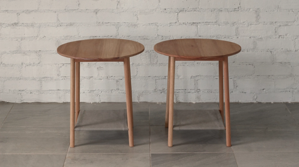 Pair of wooden side tables, round section legs, round top blueish grey fabric shelf.