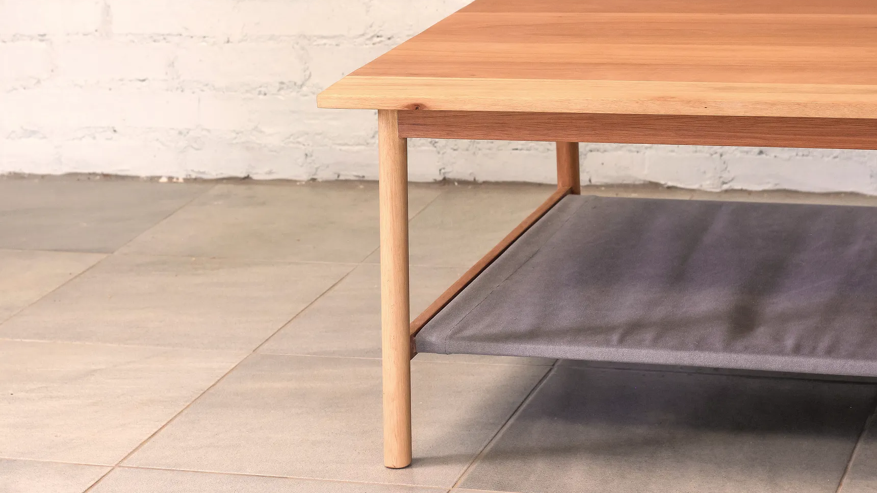 Coffee Table Detail Detail view of coffee table made from pale timber, round section legs that splay out with a fabric shelf.