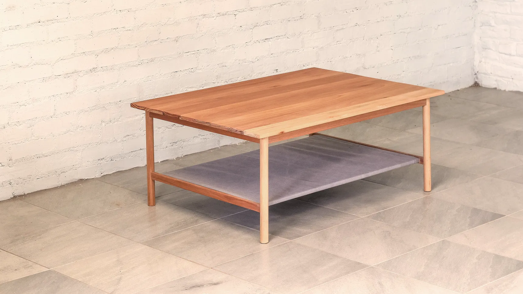 Coffee Table Three Quater Coffee table made from pale timber, round section legs that splay out with a fabric shelf.