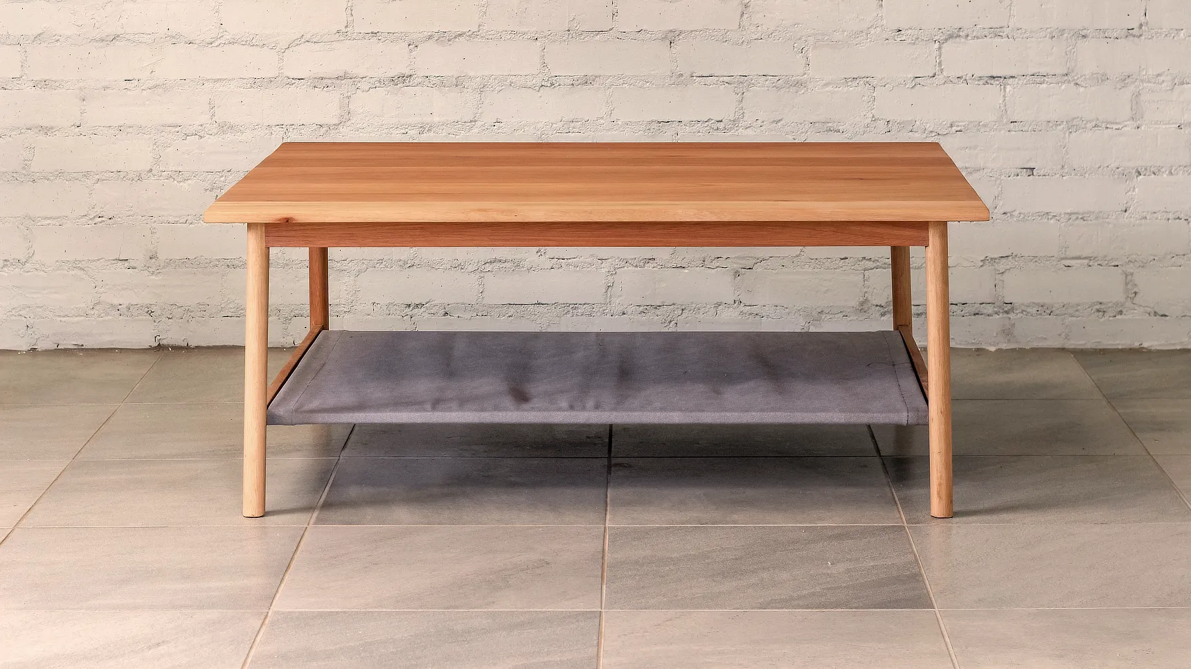 Coffee Table Coffee table made from pale timber, round section legs that splay out with a fabric shelf.