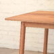 Detail of a table made from pale brown timber and round section legs.