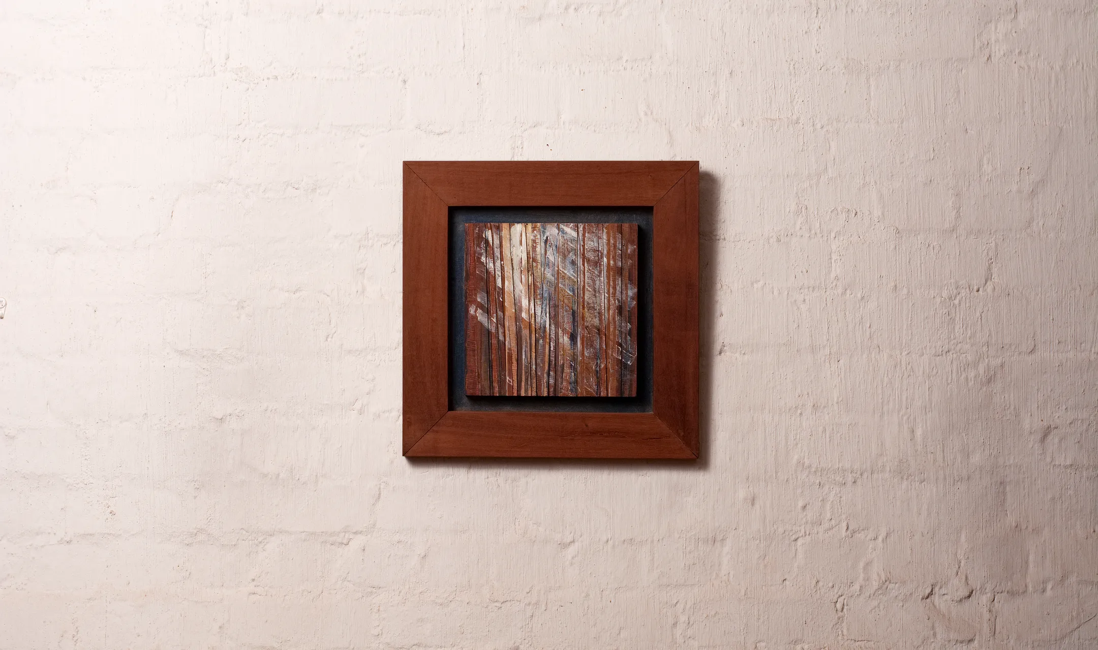 Semi abstract artwork depicting a forest with light shining through the trees in wood cuts and acrylic paint, framed with a deep blue border and brown picture frame.