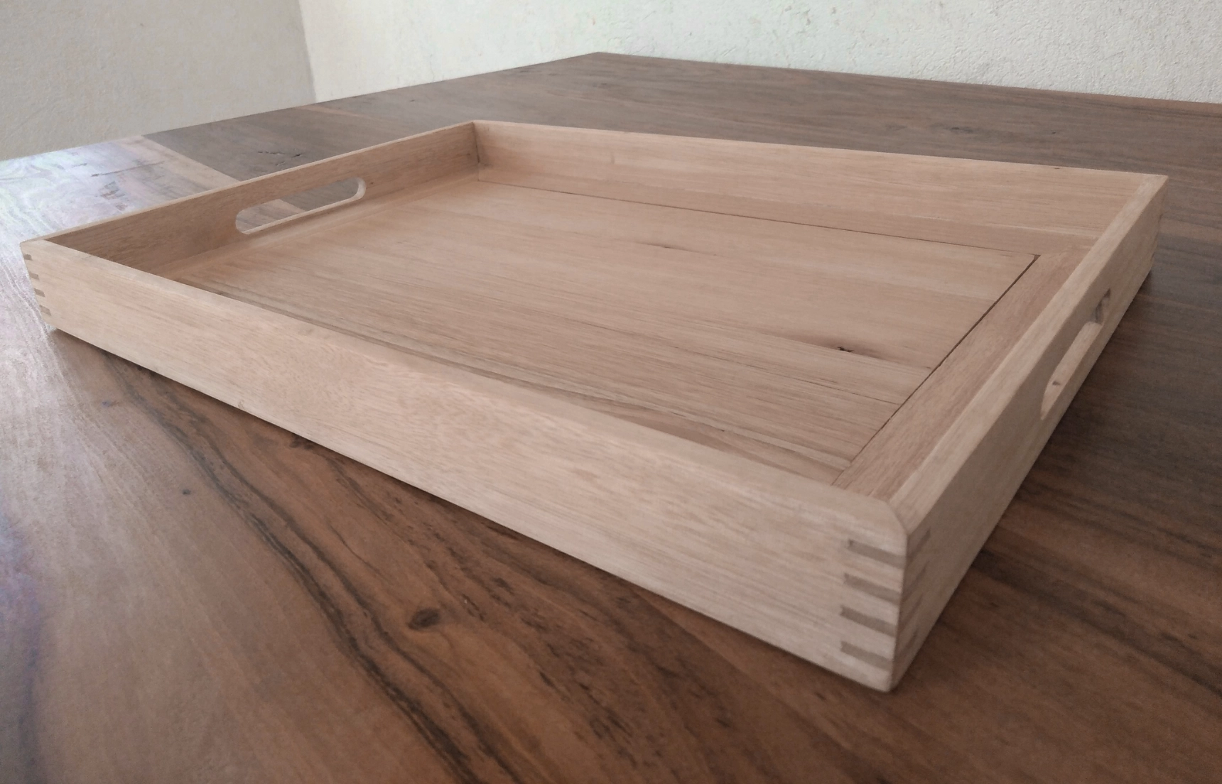 An angled shot of a tea tray made from pale timber showing the corner miter joint reinforced with splines.